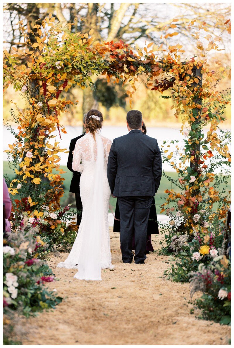 bride and groom under arbor made from fall florals and leaves at Marblegate Farm