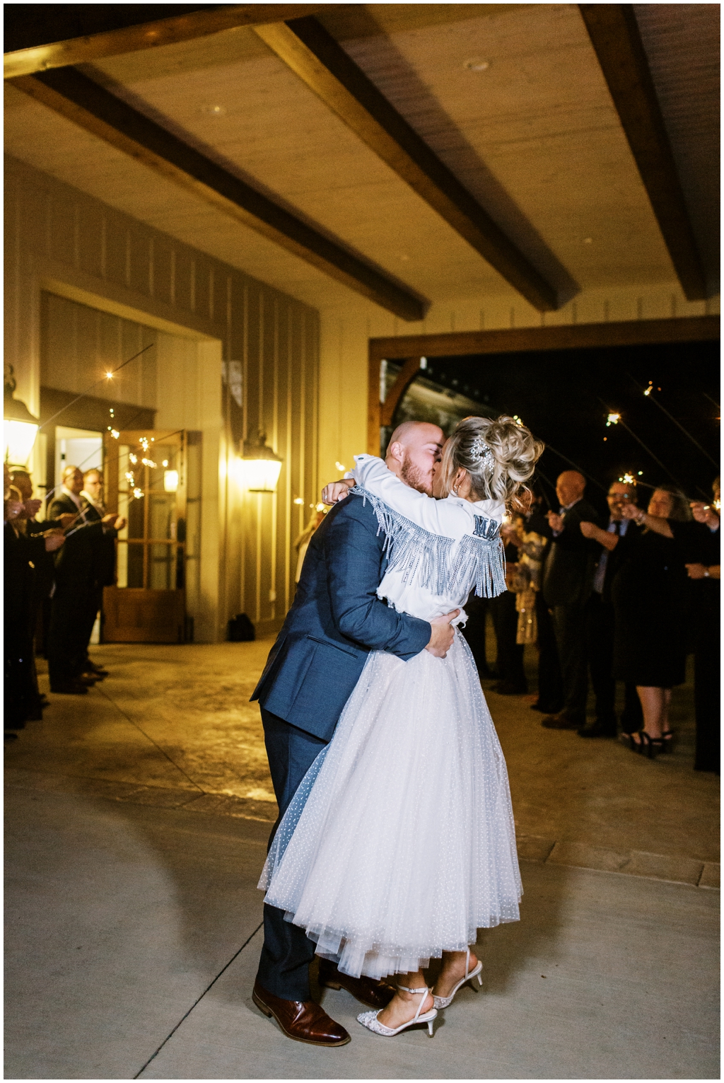 Emily Ann Roberts and Chris Sasser kiss at their sparkler exit wearing her custom leather bridal jacket.
