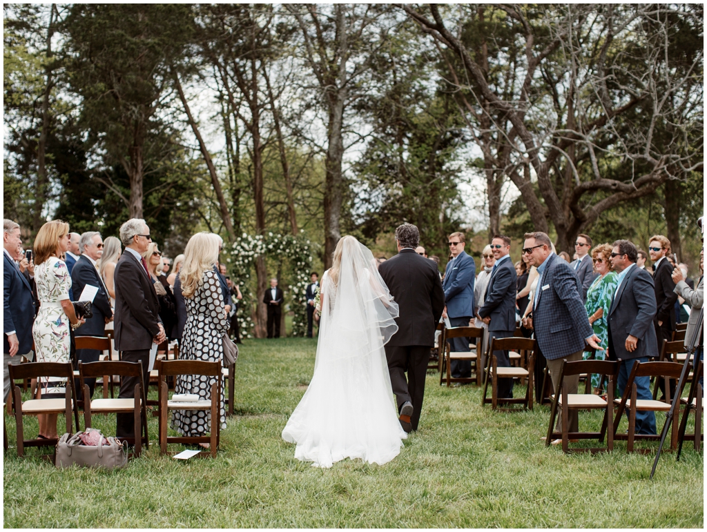 Bride and father proceed down the aisle at outdoor spring wedding